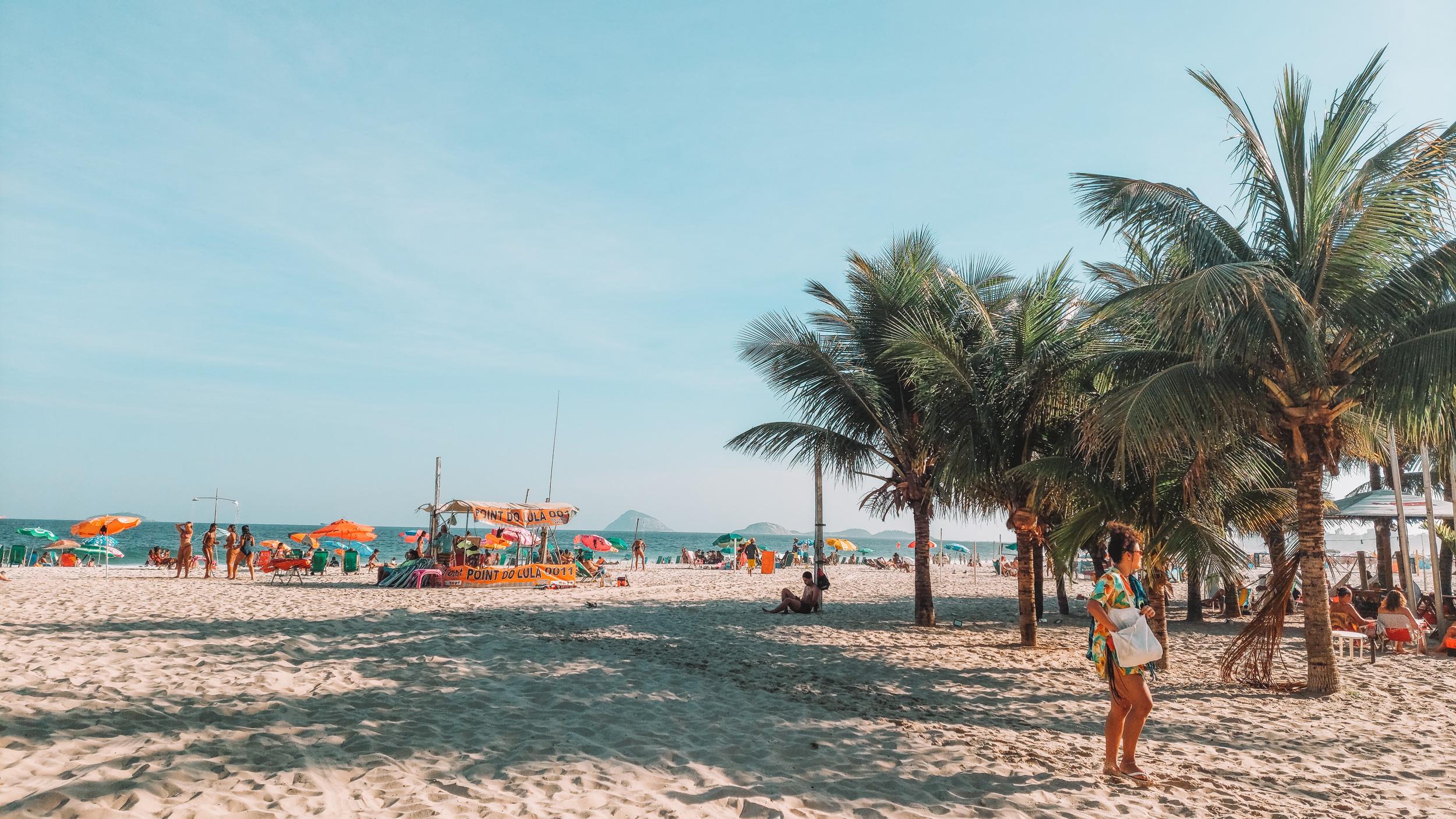 En un día soleado en Río de Janeiro, la playa de Copacabana presume de un telón de fondo de cielos y mares azules, bordeados de exuberantes palmeras verdes y repleto de personas paseando por la orilla.