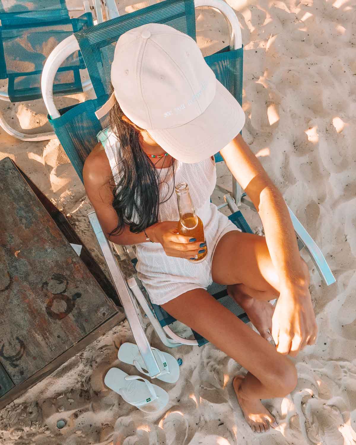 Mujer con gorra y shorts blancos bebiendo una cerveza long neck en la playa de Barra da Tijuca en Río de Janeiro.