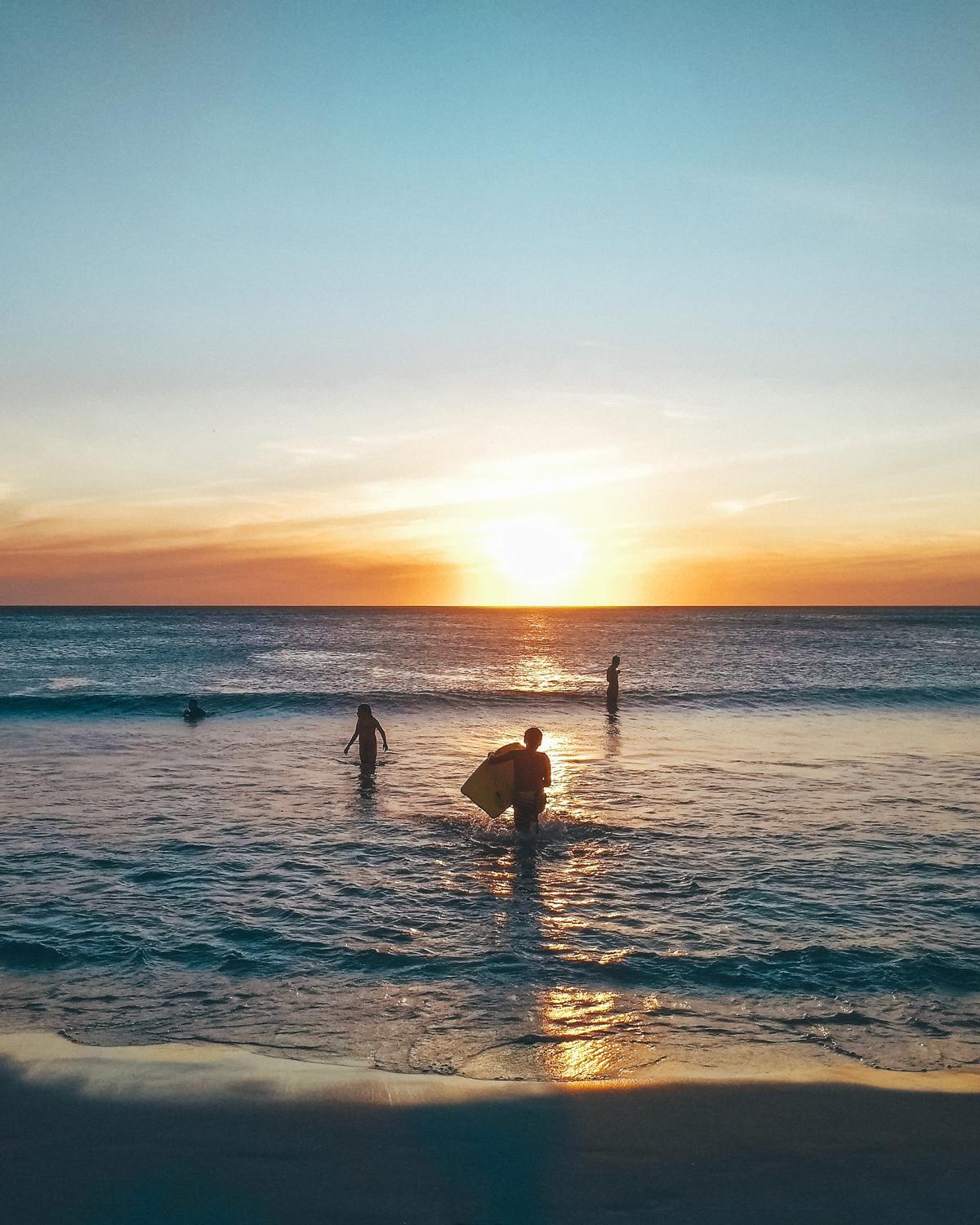 Atardecer mágico en la Playa Grande de Arraial do Cabo con personas disfrutando del agua, capturando la belleza y tranquilidad del lugar, perfecto para finalizar un día de exploración.