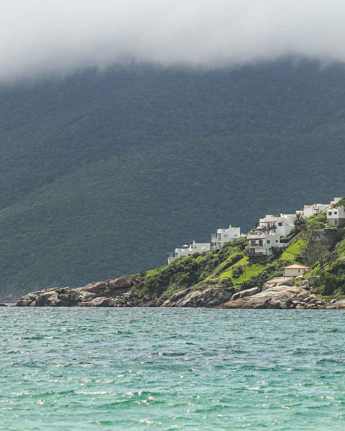 Un grupo de edificios modernos blancos con vista a las aguas azules, situados en la mejor región para alquilar casa de temporada en Arraial do Cabo, el Pontal do Atalaia.