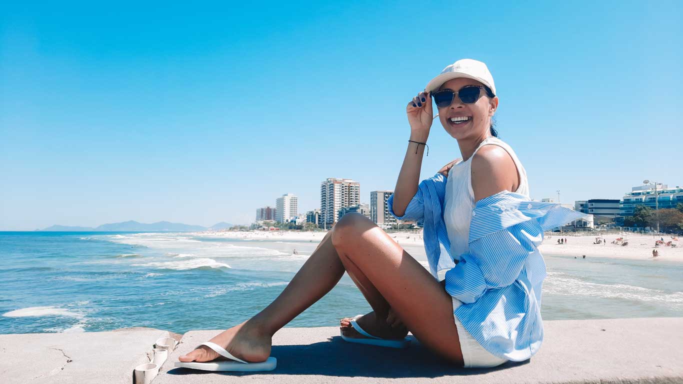Mujer sentada al borde de un muro junto a la playa de Barra da Tijuca, uno de los mejores barrios dónde alojarse en Río de Janeiro, en un día soleado.